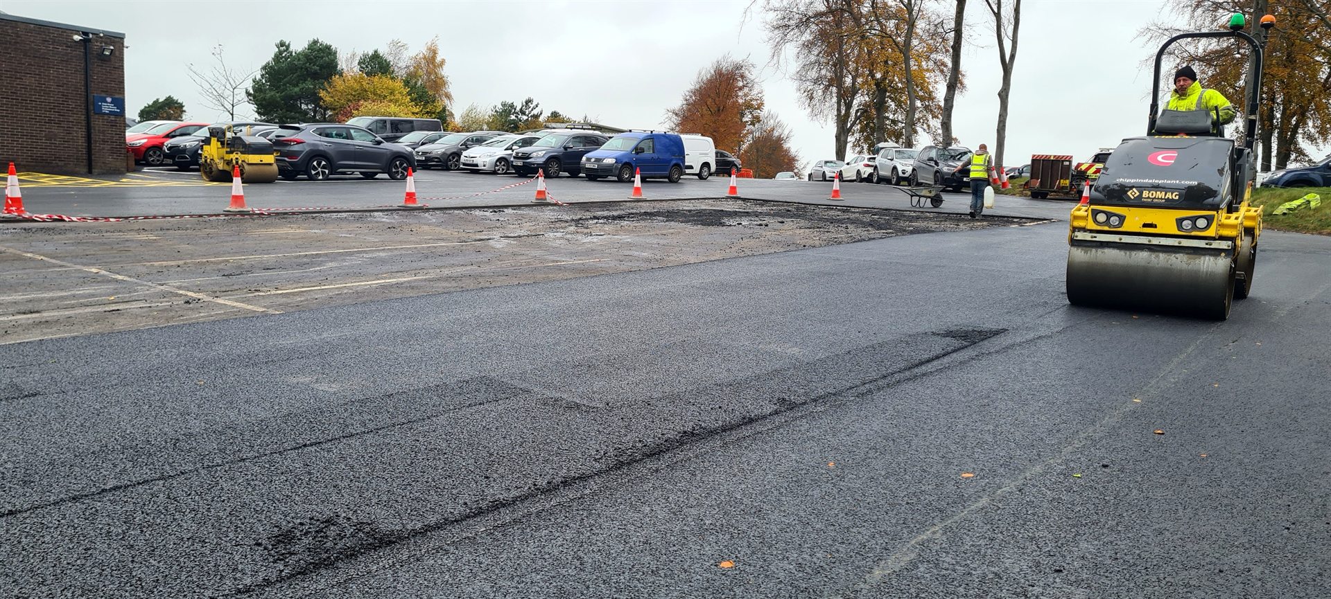 Yellow roller compacting fresh asphalt behind the paving crew